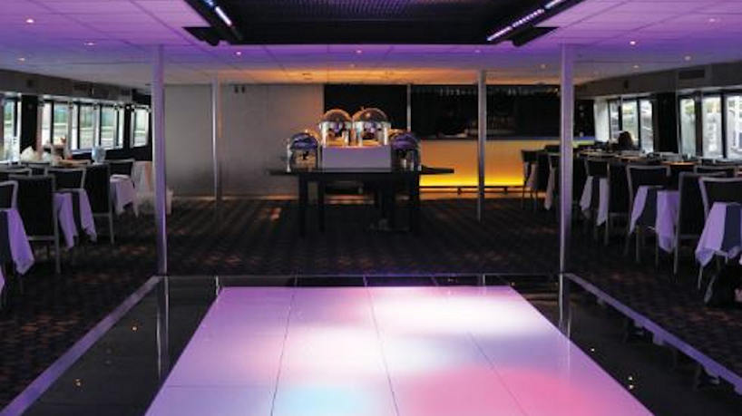 Modern yacht event space with glowing dance floor and buffet setup.